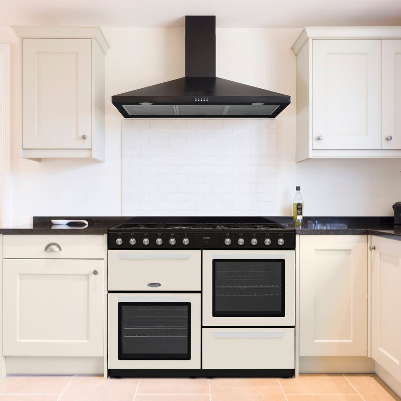 Cream Montpellier MDFRC100C 100cm dual fuel range cooker with black handles and dials, set in a modern kitchen with white. - DB Domestics